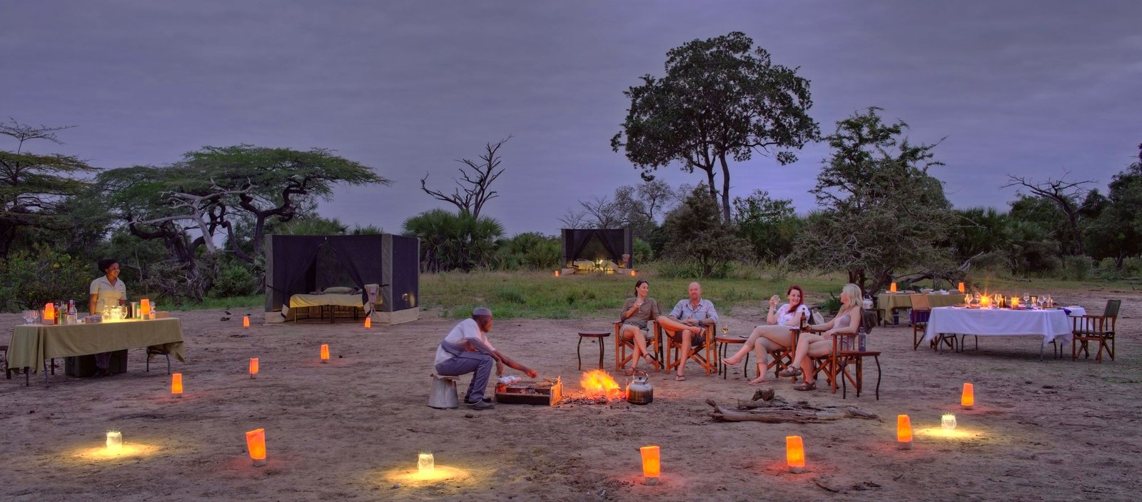 Remote luxury tented fly camp lit by a campfire under the wild canopy trees at night